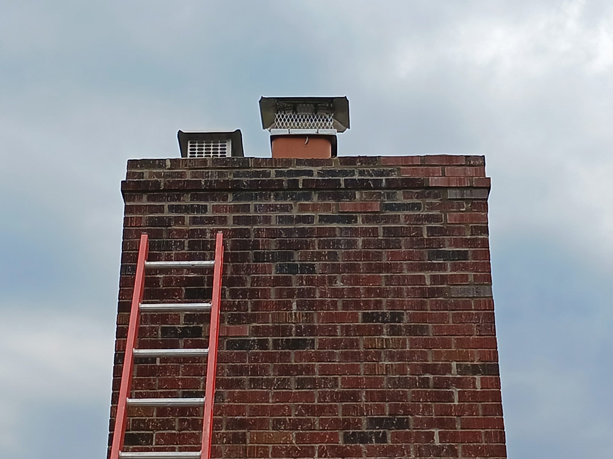 Brick chimney with red ladder and sky.