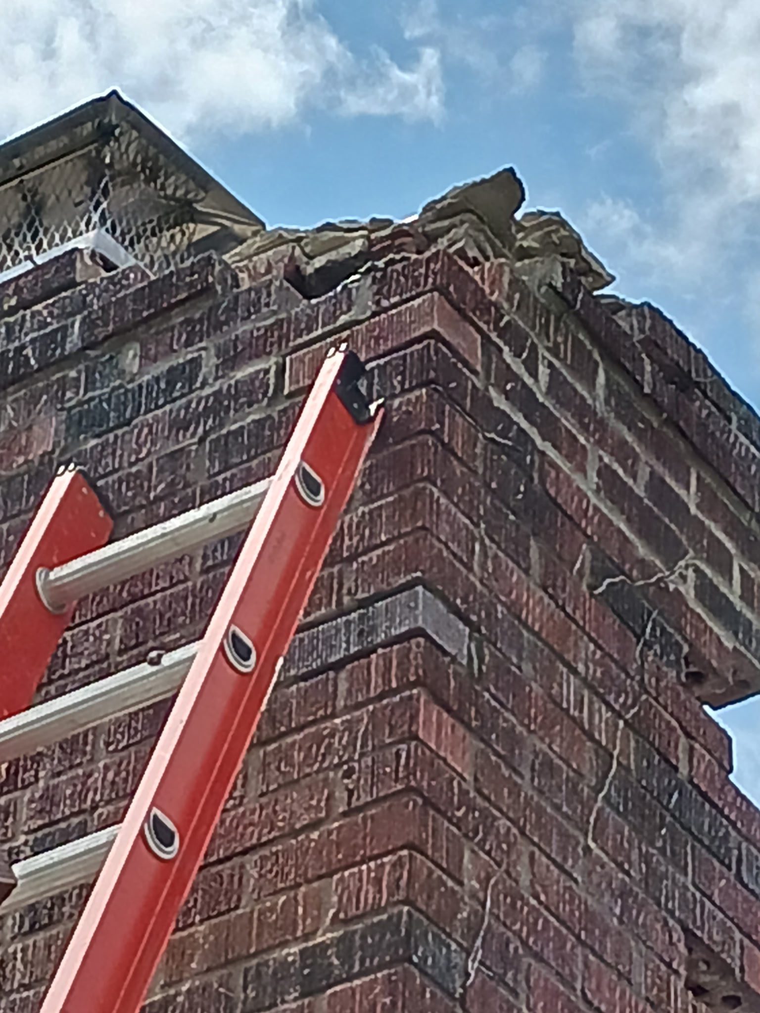 Damaged brick chimney with red ladder.