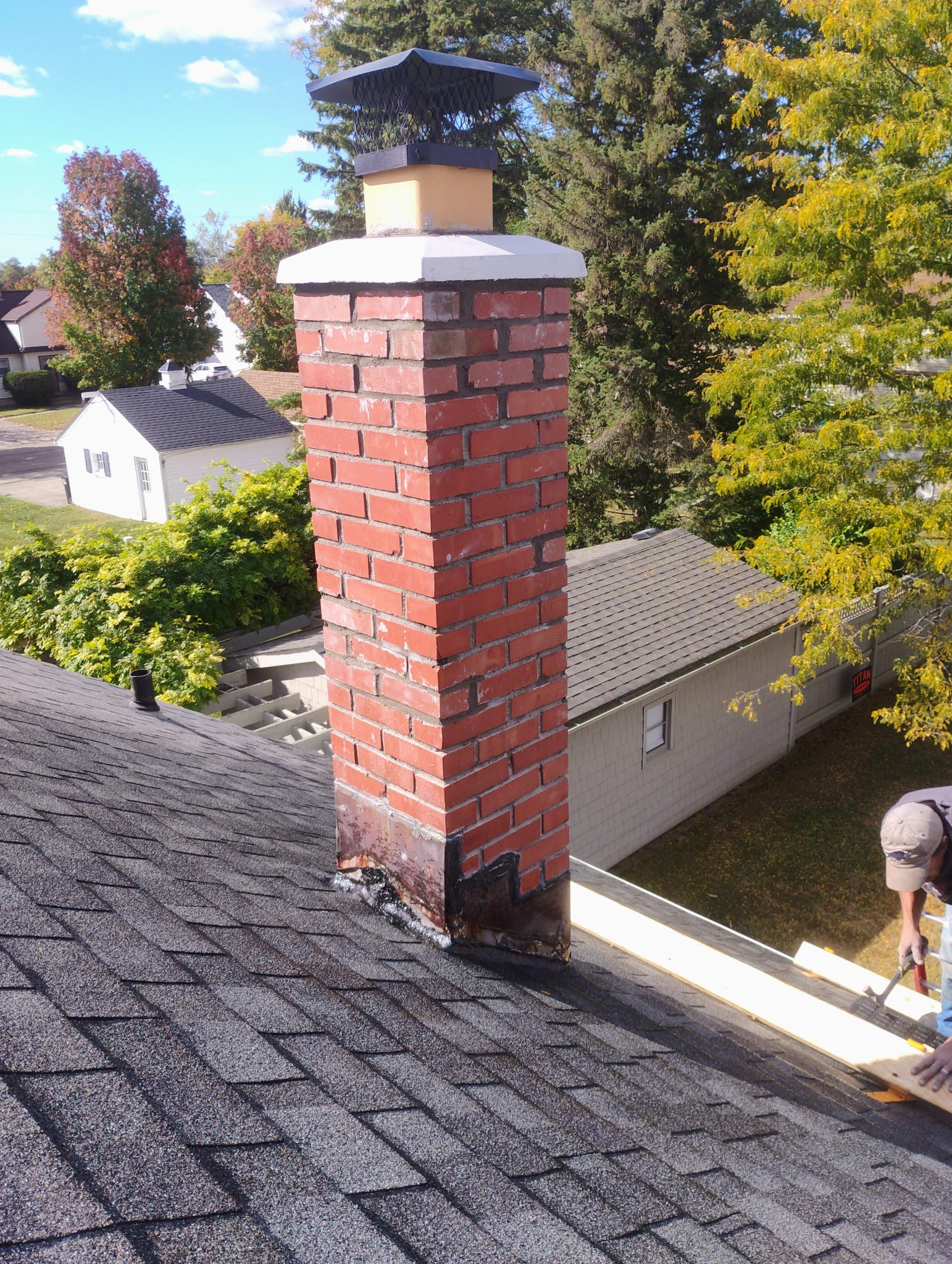 Red brick chimney on shingled rooftop.