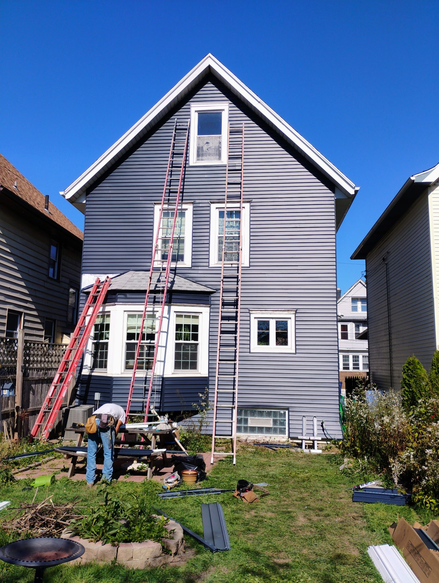 House exterior with ladders and worker outside.