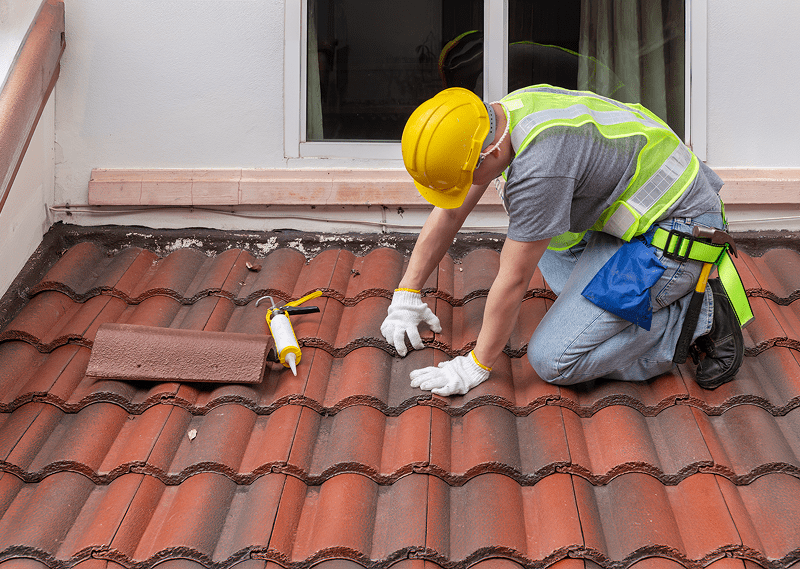 Worker repairing roof with tiles and tools.