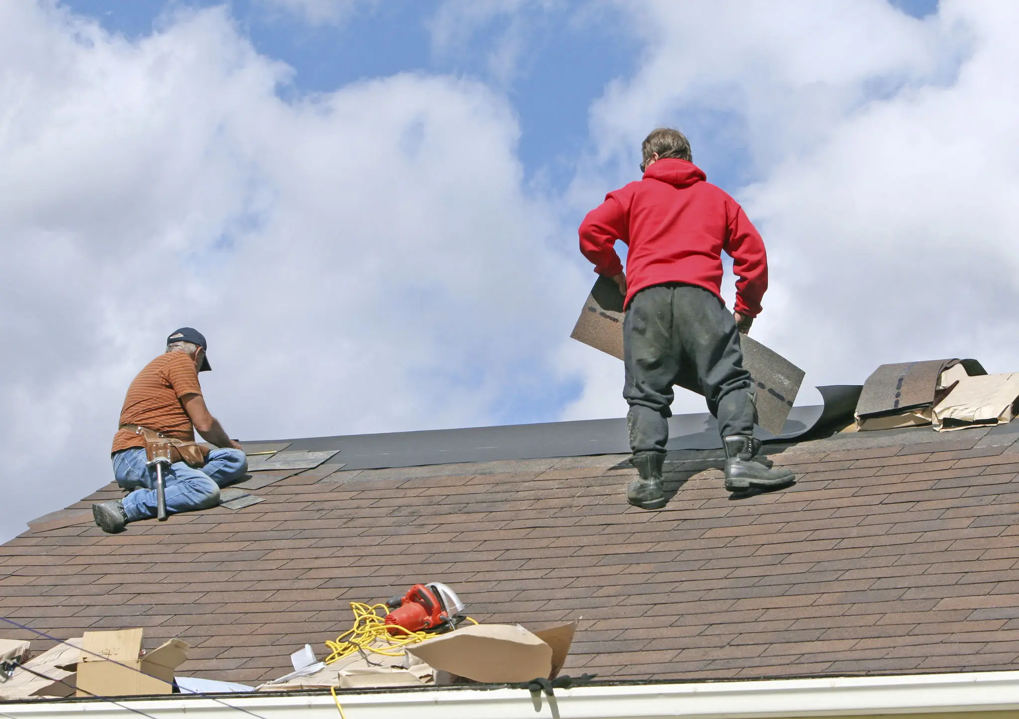 Workers repairing a roof under cloudy sky.