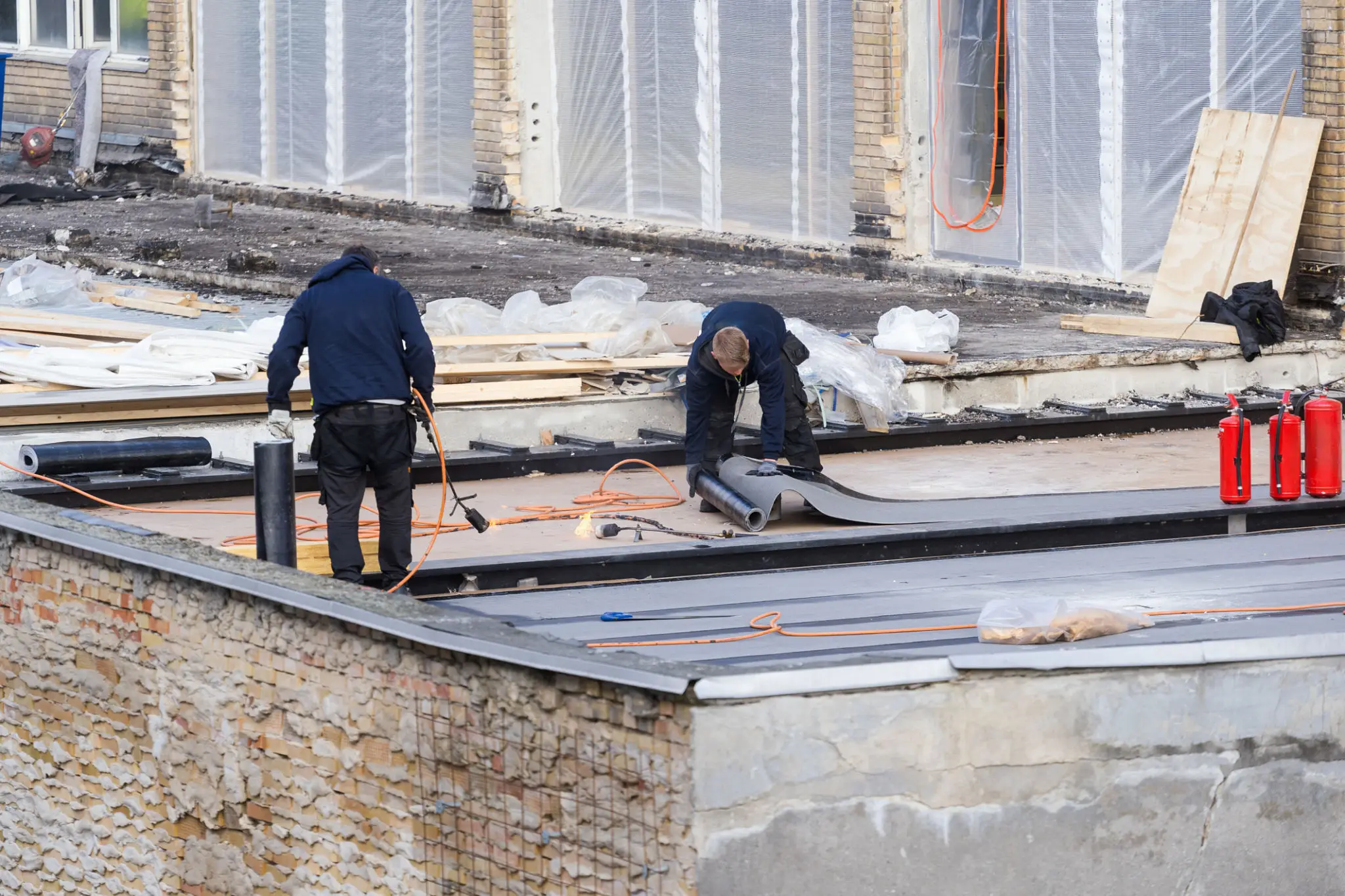 Workers installing roofing materials on building roof.